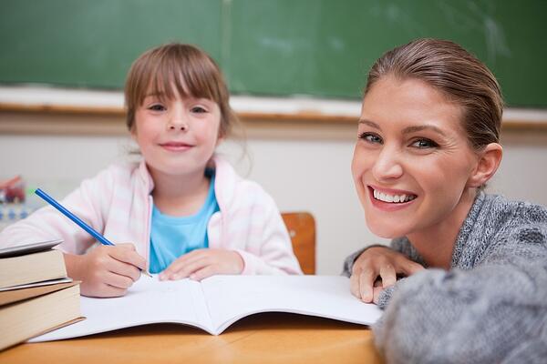 Schoolgirl writing with her teacher in a classroom